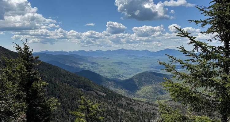 Vue panoramique sur les chaînes de montagnes des Adirondacks et les vallées boisées sous des nuages cotonneux.