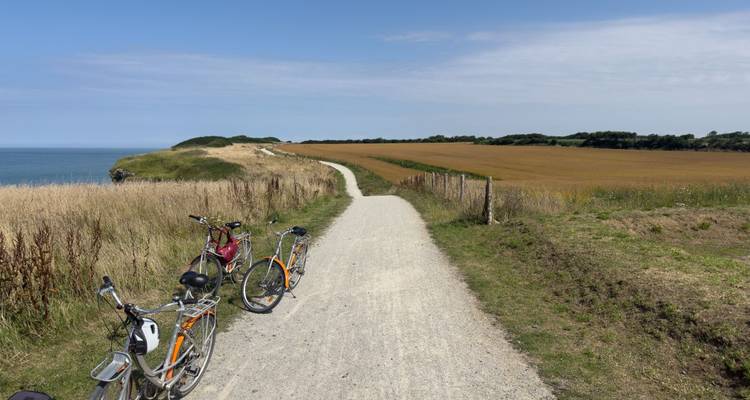 Piste cycliste en gravier au sommet des falaises côtières avec deux bicyclettes garées surplombant les champs et la mer.