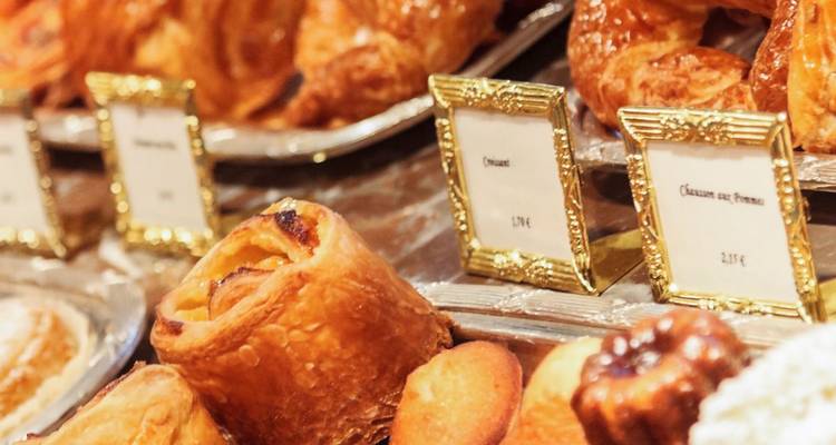 Gros plan de pâtisseries françaises dorées et d'étiquettes de prix sur un plateau d'exposition de boulangerie.