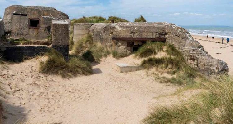 Bunker en béton de la Seconde Guerre mondiale, usé par le temps, à moitié enfoui dans les dunes de sable le long d'une vaste plage déserte.
