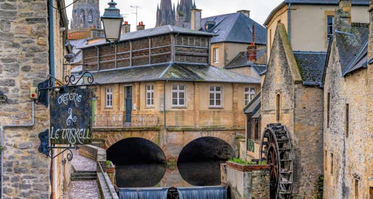 Des bâtiments en pierre de charme et à colombages enjambent un canal sous les flèches de la cathédrale de Bayeux.