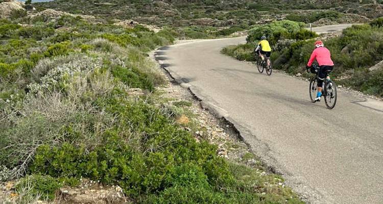 Cyclists climb a winding rural road through rocky scrubland on the Costa Brava.