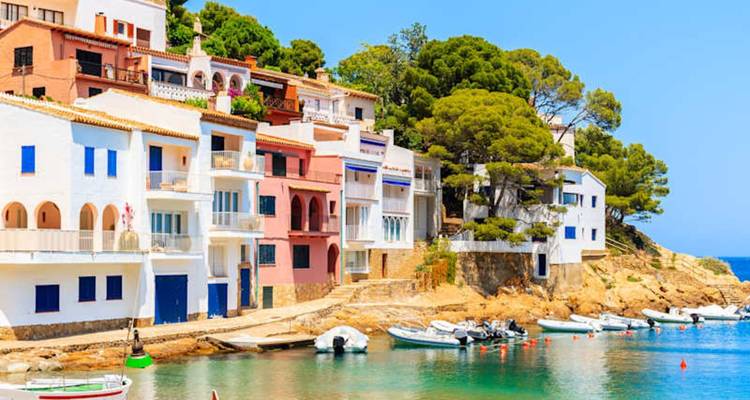 Row of pastel Mediterranean houses facing a tranquil harbor with boats on the Costa Brava.