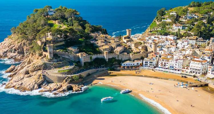 Aerial view of Tossa de Mar’s medieval walled fortress overlooking a golden beach and turquoise sea.