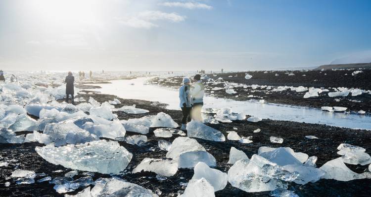 Glittering ice blocks scattered across the black sands of Diamond Beach with visitors exploring the shoreline.