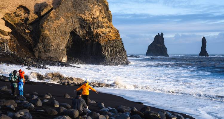 Tourists on the black sands of Reynisfjara beach with dramatic basalt cliffs and Reynisdrangar sea stacks.