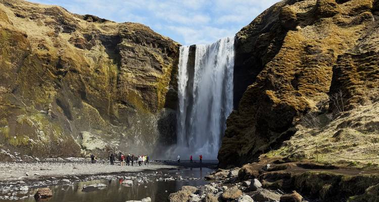Visitors standing near the base of majestic Skógafoss waterfall cascading over mossy cliffs.