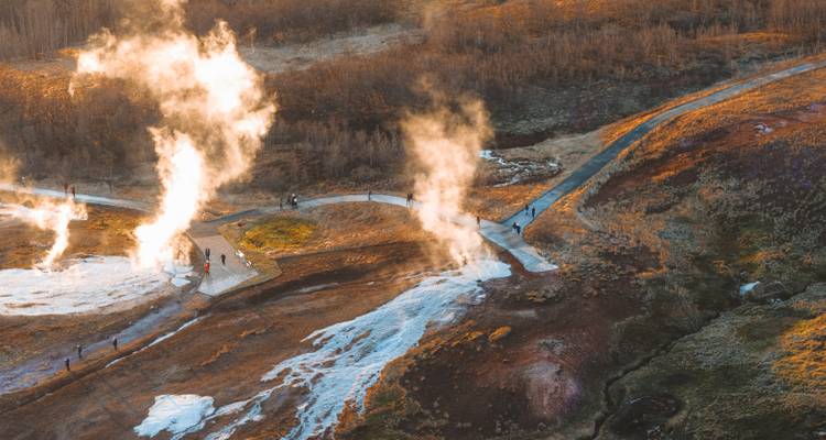 Aerial scene of steaming geysers and winding boardwalks at sunrise in Iceland’s geothermal valley.