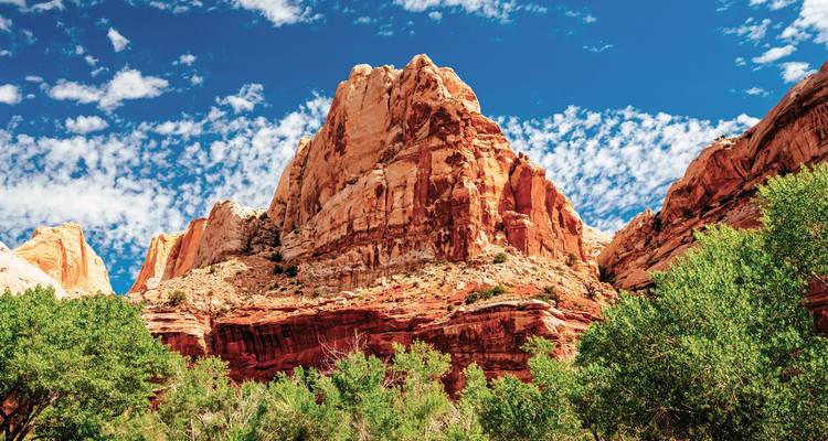 Rote Sandsteinklippen und Grünflächen unter einem punktierten Himmel im Capitol Reef