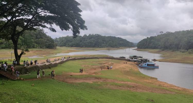 Besucher spazieren entlang des Seeufers mit vertäuten Booten inmitten üppiger Hügel innerhalb des Periyar-Tigerreservats.