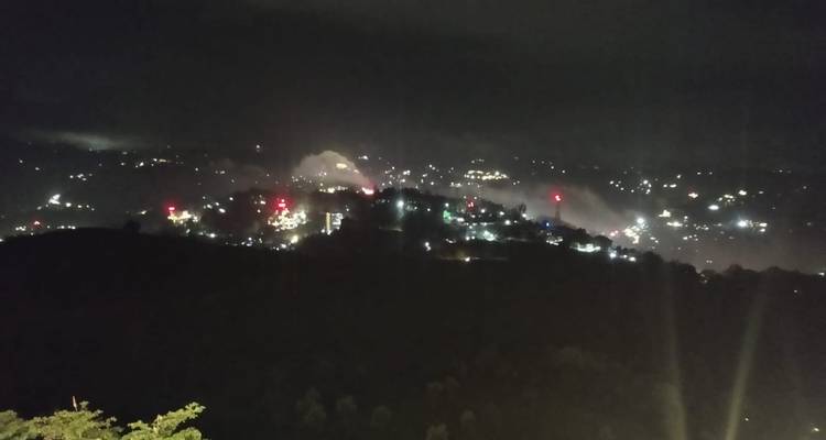 Verschwommene nächtliche Hügellandschaft einer Stadt mit verstreuten Lichtern unter dunklem Himmel.