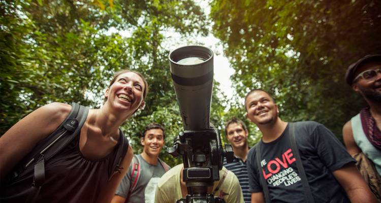 Excited travelers gather around a spotting scope during a rainforest wildlife walk.