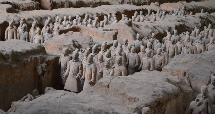 Filas de Guerreros de Terracota de tamaño natural se encuentran en trincheras excavadas, su armadura detallada y expresiones visibles bajo la suave iluminación del museo.