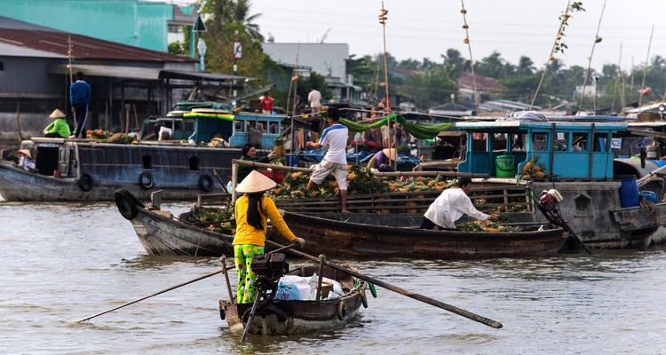 Des petits bateaux commerciaux convergent vers une scène animée de marché flottant en bord de rivière.
