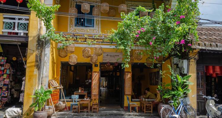 Facade pittoresque d'un cafe a Hoi An peinte en jaune avec des vignes, des lanternes et un seul client assis a l'interieur.