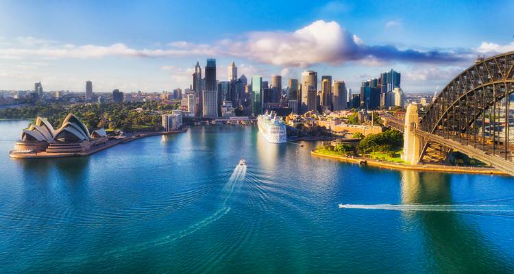 Hochfliegende Luftaufnahme des Sydneyer Hafens mit Opernhaus, Harbour Bridge und Kreuzfahrtschiff unter dramatischer Wolkenbank