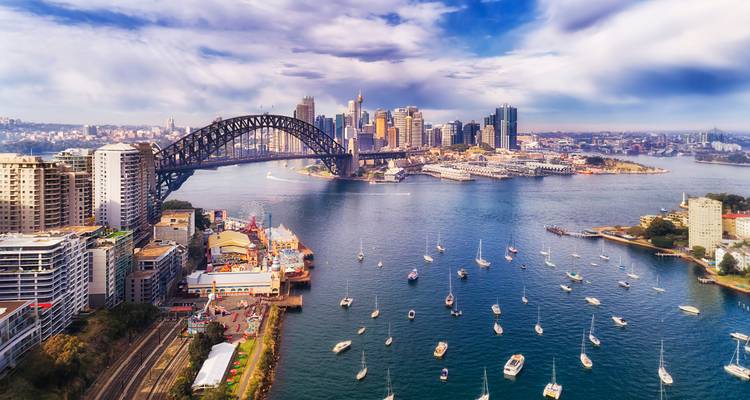 Drohnenaufnahme in Richtung Sydney Harbour Bridge, Skyline der Stadt und gehäufte Segelboote auf glitzerndem blauen Wasser