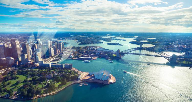 Breite Luftaufnahme des Sydney Harbour mit Opernhaus, Hafenbrücke und gewundenen Wasserwegen unter verstreuten Wolken