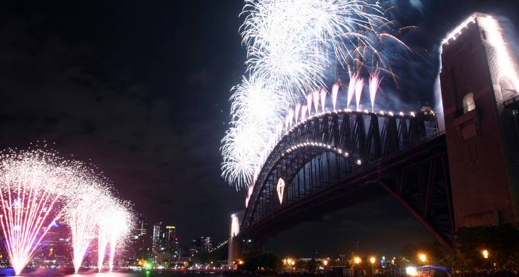 Spectacle de feux d'artifice nocturnes se déversant du Pont du Port de Sydney avec des gerbes de couleurs se reflétant sur l'eau