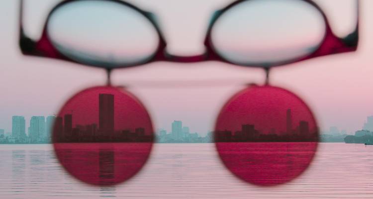 Creatieve weergave van de skyline van Hanoi door roze getinte zonnebrillen die voor een pastelkleurige lucht worden gehouden.