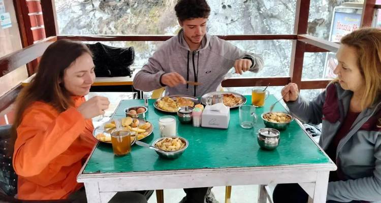 Trekkistas disfrutando de una comida abundante en una mesa de una simple casa de té durante una caminata en Nepal.