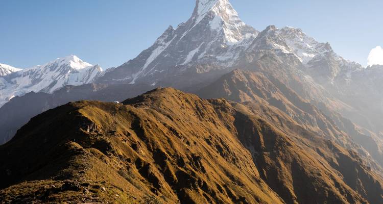 Cresta iluminada por el sol del macizo de Machhapuchhre con picos afilados elevándose sobre laderas marrones y escarpadas.