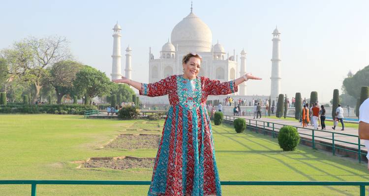 Reisende in gemustertem Kleid mit ausgestreckten Armen vor den Gärten des Taj Mahal.
