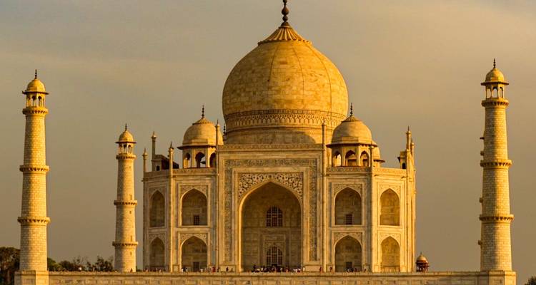 Le Taj Mahal illuminé d'or vu de face à travers la rivière Yamuna au coucher du soleil, avec de minuscules visiteurs à sa base.