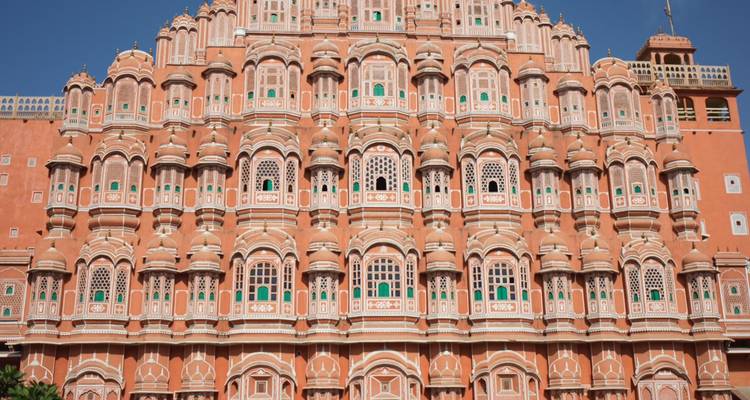Vue frontale symétrique du Hawa Mahal en grès rose aux nombreuses fenêtres sous un soleil éclatant.
