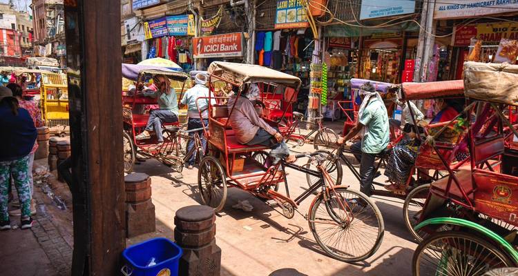 Rue animée de Delhi remplie de pousse-pousse à pédales rouges, de vendeurs et de devantures de magasins colorées.
