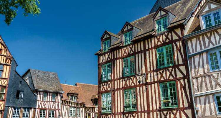 Rangée de maisons médiévales à colombages avec des fenêtres à cadre vert sous un ciel bleu dégagé.