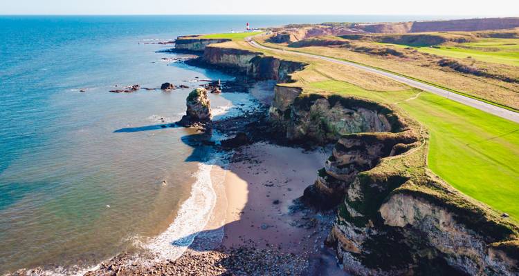 Un autre angle de la côte accidentée de Normandie avec des criques sablonneuses et des falaises à côté d'une mer bleu profond.