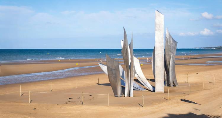 Vue latérale de la sculpture commémorative Les Braves sur le large sable avec la mer calme au-delà.