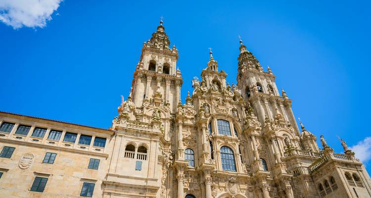 Barocke Türme und detaillierte Steinmetzarbeiten der Kathedrale von Santiago de Compostela, die sich gegen einen klaren blauen Himmel erheben