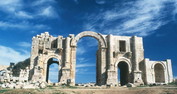 Oude driedubbele stenen poort van een Romeinse ruïne staat tegen een felblauwe hemel.