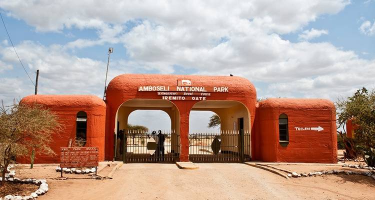 Puerta de entrada del Parque Nacional de Amboseli pintada en tonos naranjas tierra bajo nubes dispersas.