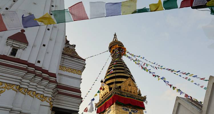 Des drapeaux de prière colorés flottent autour d'une flèche de stupa doré contre un ciel pâle