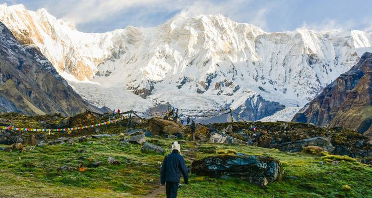 Le trekker s'approche des drapeaux de prière colorés sous le spectaculaire mur de neige du Sanctuaire de l'Annapurna
