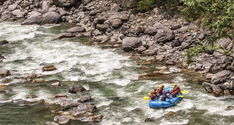 Raft with paddlers navigates white-water rapids between boulders on a mountain river