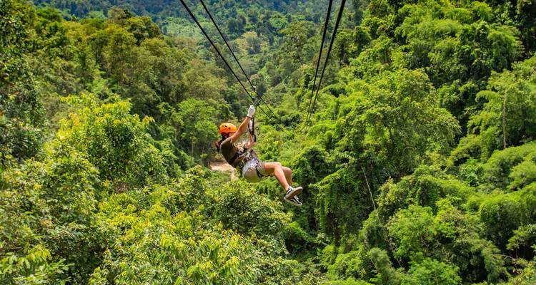 L'aventurier descend en tyrolienne au-dessus de la canopée dense de la jungle cambodgienne en portant un casque orange