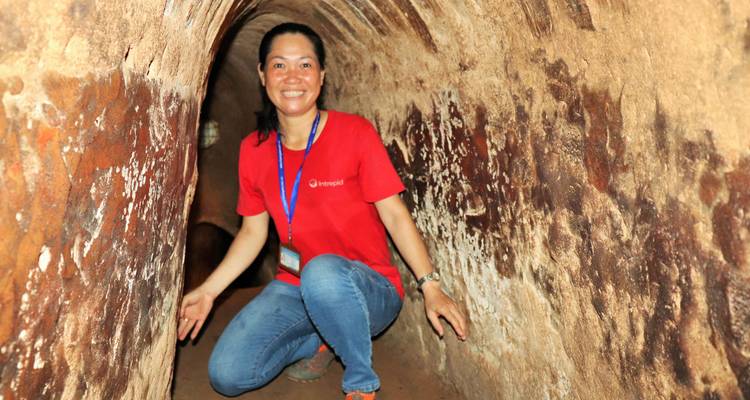 Le visiteur s'accroupit dans le réseau étroit de tunnels souterrains de Cu Chi en souriant à l'appareil photo