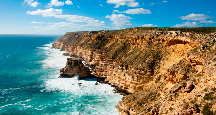 Des falaises de grès spectaculaires plongent dans des vagues turquoise le long d'un littoral accidenté sous des nuages épars.