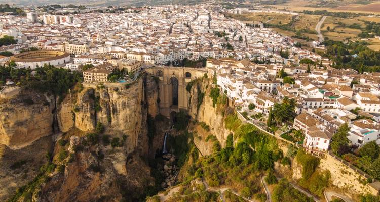 Vue aérienne élevée de Ronda montrant l'arène de corrida, le Puente Nuevo et la ville blanche s'étendant sur un plateau accidenté.