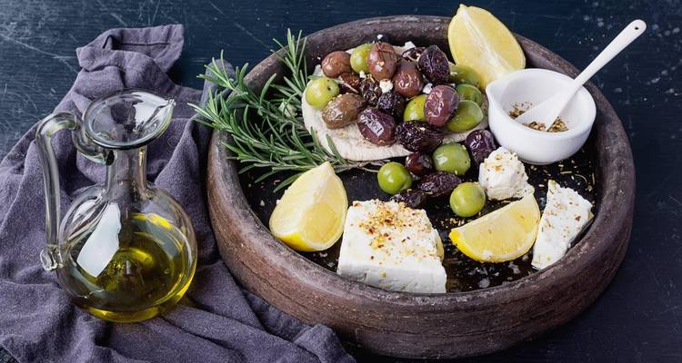 Rustieke schotel met feta, olijven, citroenpartjes, rozemarijn en olijfolie op donkere achtergrond.