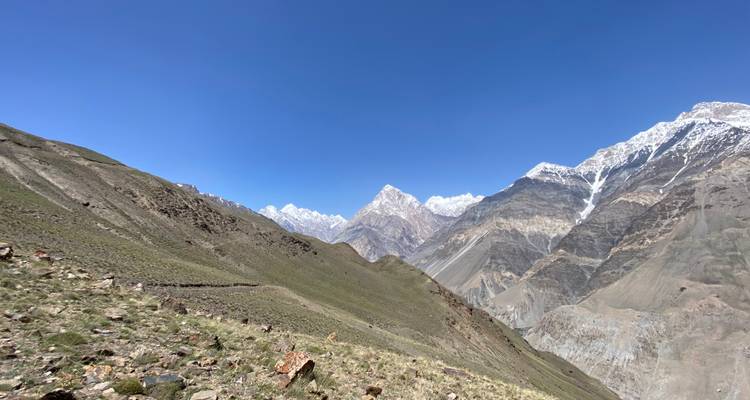 Snow-capped peaks rise sharply above an arid alpine slope beneath a flawless blue sky.