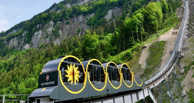 Ferrocarril inclinado con marca Victorinox subiendo por una dramática pista en el acantilado boscoso.