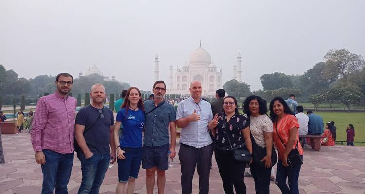 Reisende stehen zusammen vor dem verschwommenen Taj Mahal an einem bewölkten Nachmittag.