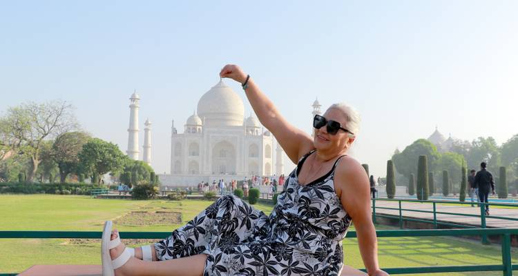 Eine Frau zwickt verspielt die Kuppel des Taj Mahal, während sie auf einer Bank in heller Sonneneinstrahlung sitzt.