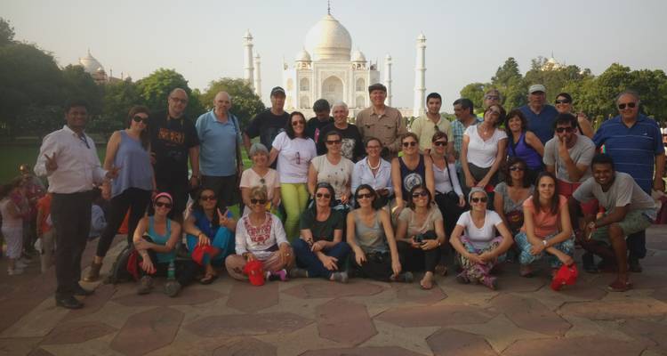 Große Reisegruppe, die auf einer Steinterrasse posiert, während sich das weiße Marmor-Taj Mahal an einem hellen, klaren Tag hinter ihnen erhebt.