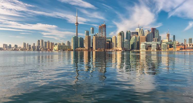 Breite Wasserfrontansicht der Skyline von Toronto, die sich in dem ruhigen Lake Ontario unter streifigen Morgenvolken spiegelt.